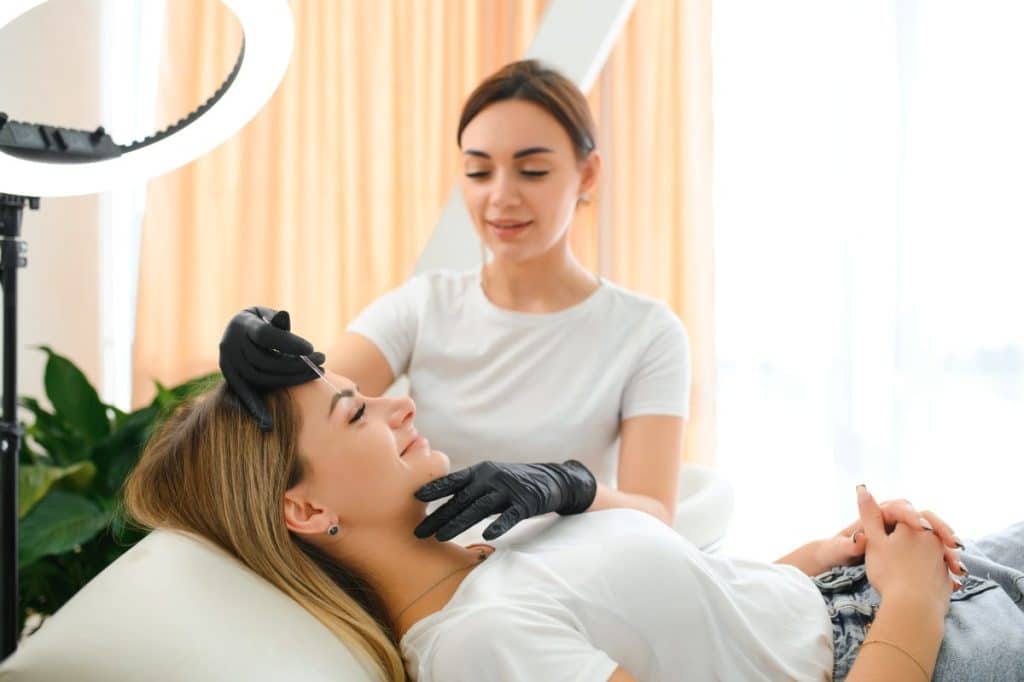 beautiful aesthetics practitioner working on a client's eyebrows